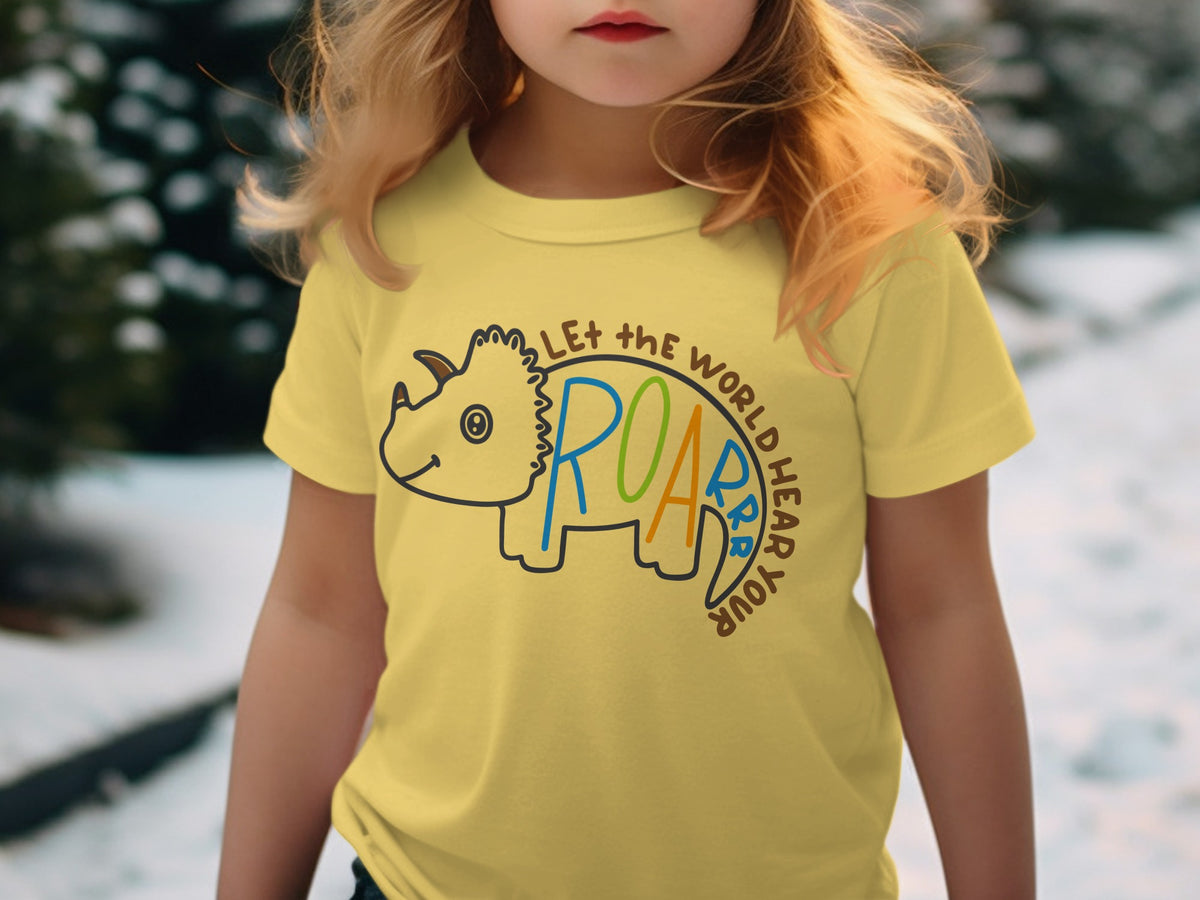 A young child wears a yellow t-shirt featuring a dinosaur graphic and the text Let the world hear your roar.