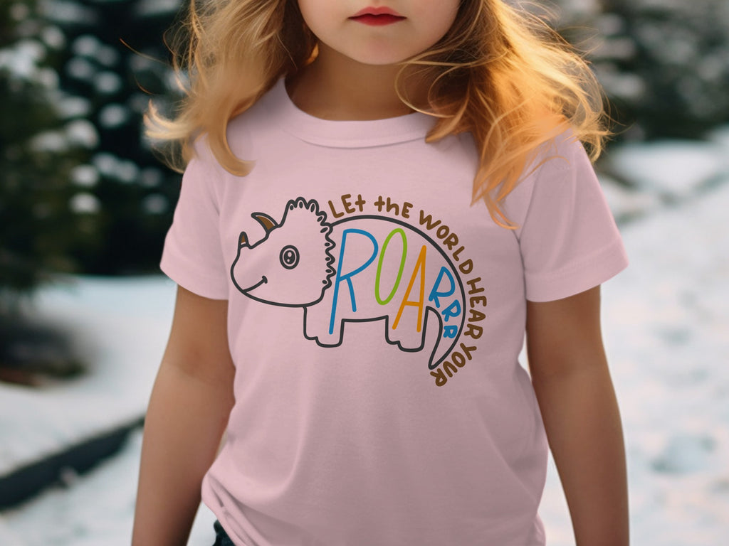 A young blonde girl wears a pink t-shirt featuring a triceratops and text reading Let the world hear your roar.