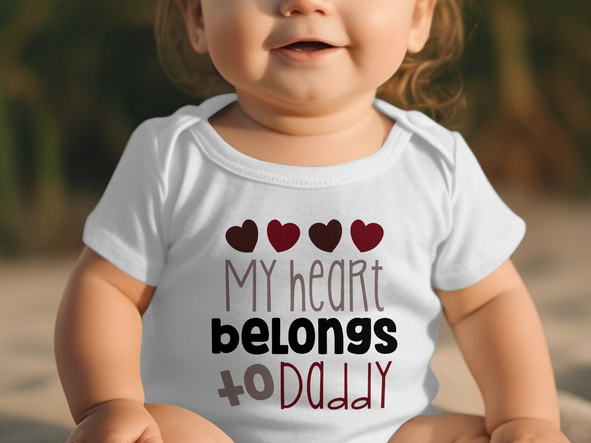 A baby wears a white bodysuit printed with four red hearts and the text My heart belongs to daddy.