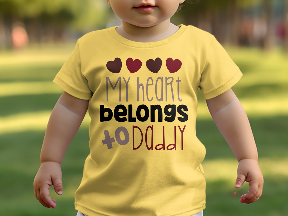 A toddler wears a yellow t-shirt printed with four hearts and the text My heart belongs to daddy.