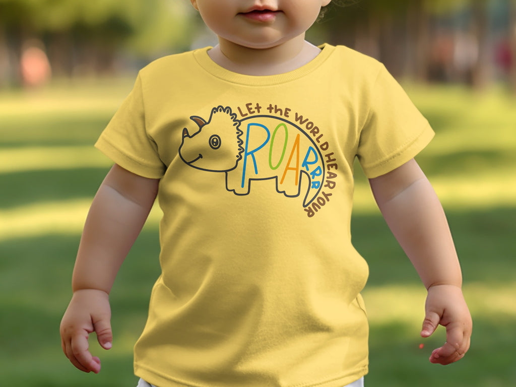 A toddler wearing a yellow t-shirt with a triceratops graphic and the text "Let the world hear your roar".