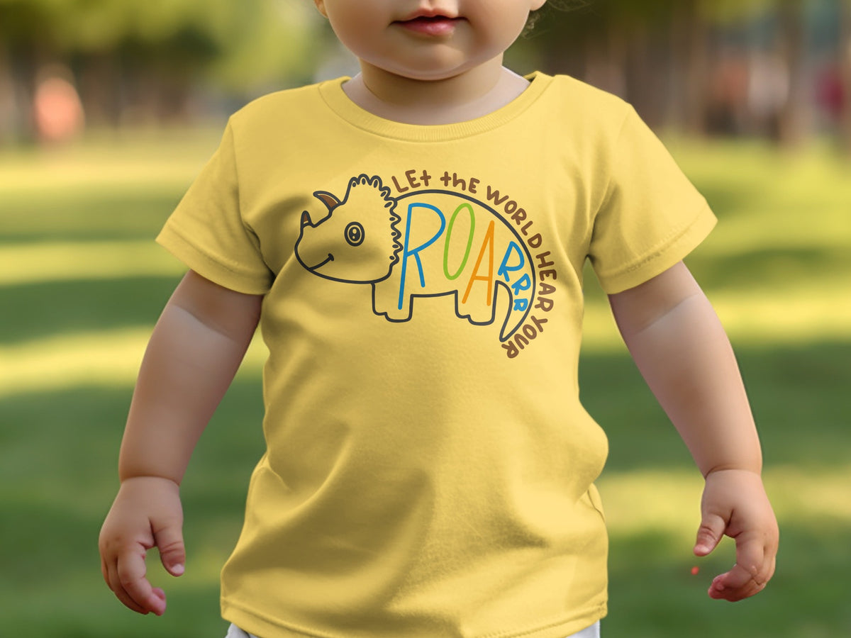 A toddler wearing a yellow t-shirt with a triceratops graphic and the text "Let the world hear your roar".