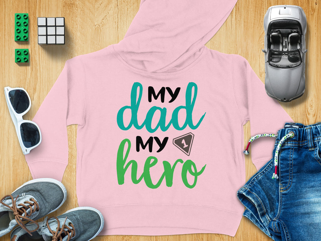 A light pink children's hoodie with text reading My dad my hero surrounded by toys.