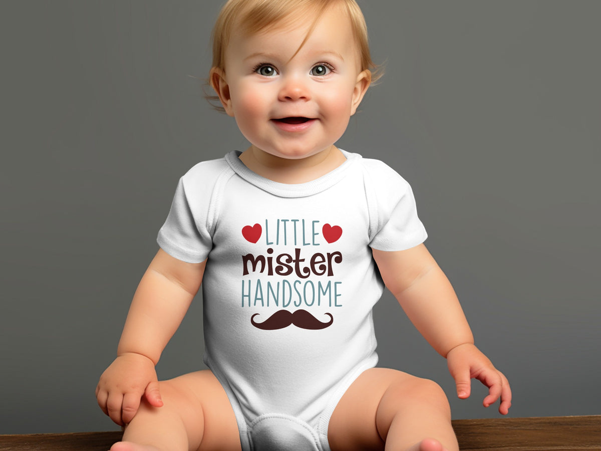 A smiling baby wearing a white bodysuit printed with the words Little Mister Handsome and a brown mustache.