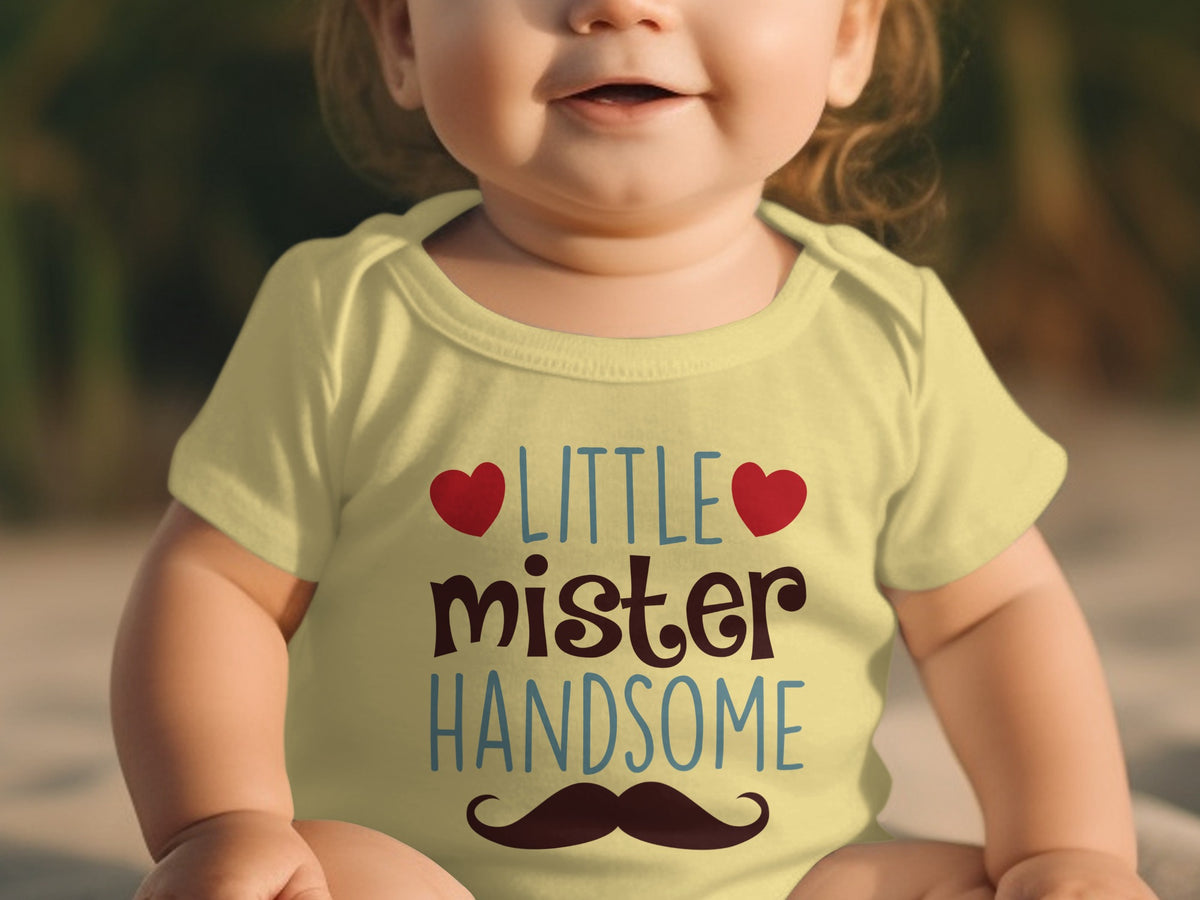 A baby wearing a yellow bodysuit printed with the words "LITTLE mister HANDSOME" flanked by two red hearts and a brown mustache.