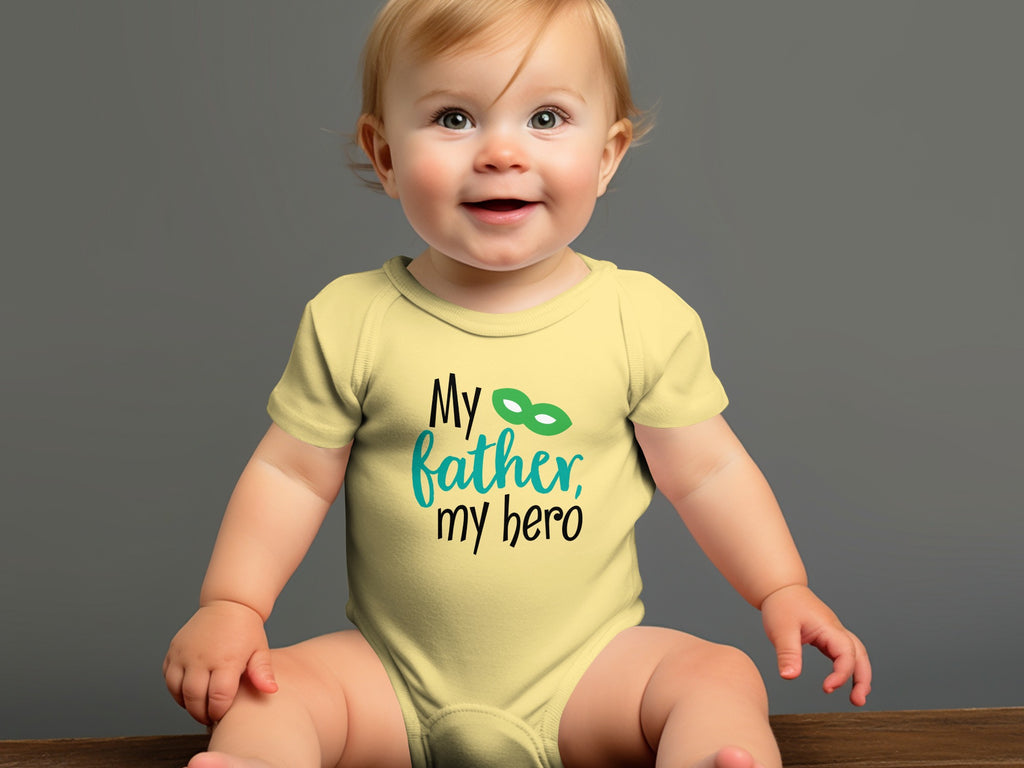 A smiling baby wearing a yellow bodysuit printed with the text My father, my hero.