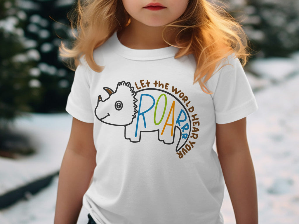 A young girl wearing a white t-shirt featuring a dinosaur graphic and the text Let the world hear your roar.