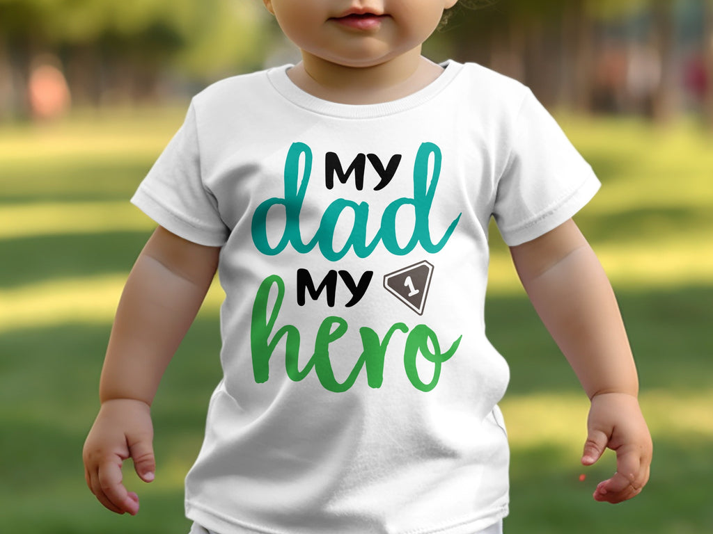 A toddler wears a white t-shirt printed with the text My Dad My Hero.