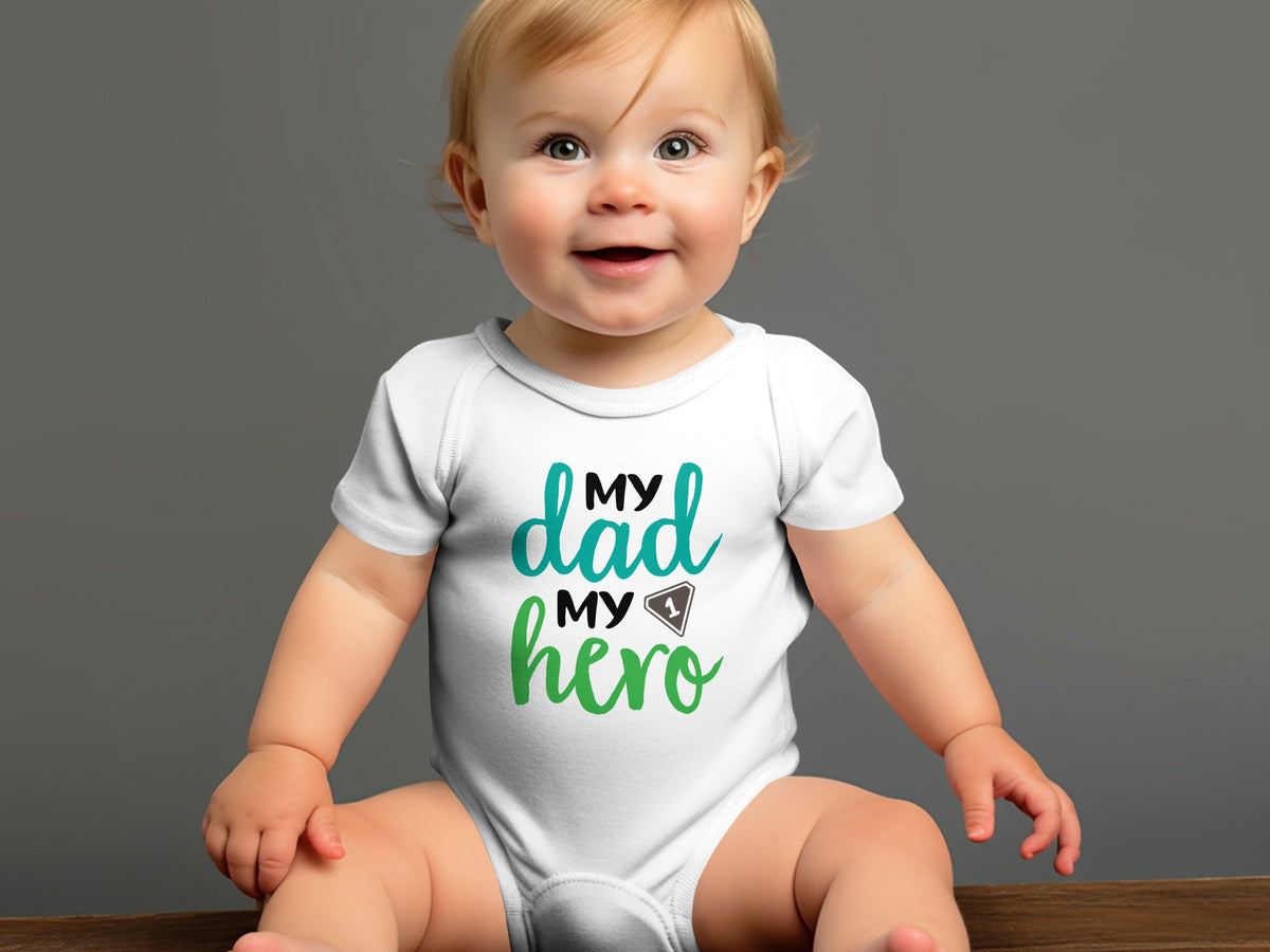 A smiling baby sits wearing a white short-sleeve bodysuit with the text My Dad My Hero printed on the chest.