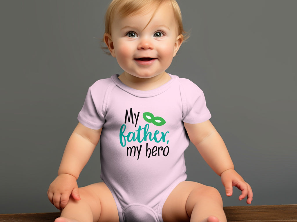 A smiling baby wearing a light pink onesie that reads My father, my hero with a green superhero mask.