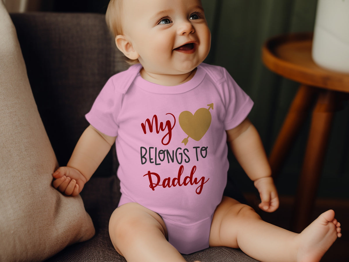 A smiling baby wearing a pink bodysuit with the text "My Heart Belongs to Daddy."
