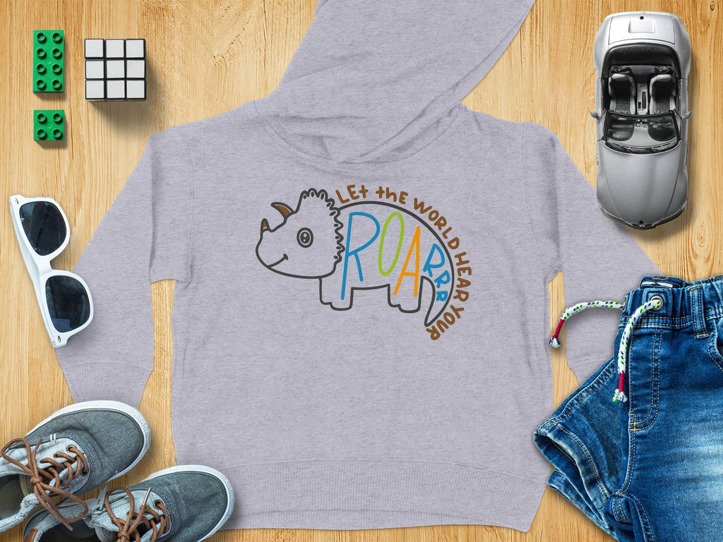 Gray children's hoodie featuring a triceratops outline and text, surrounded by toys and accessories on wood.