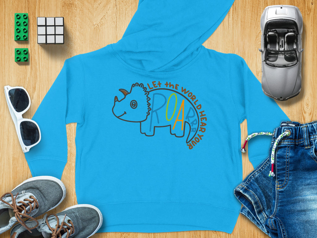 Bright blue children hoodie with a triceratops graphic and the text Let the World Hear Your Roar surrounded by toys.