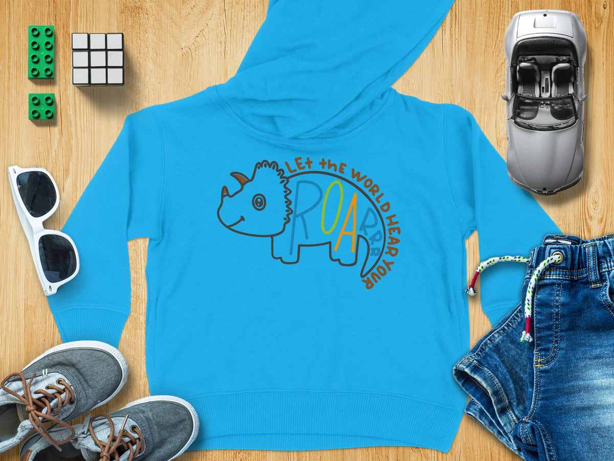 Bright blue children hoodie with a triceratops graphic and the text Let the World Hear Your Roar surrounded by toys.