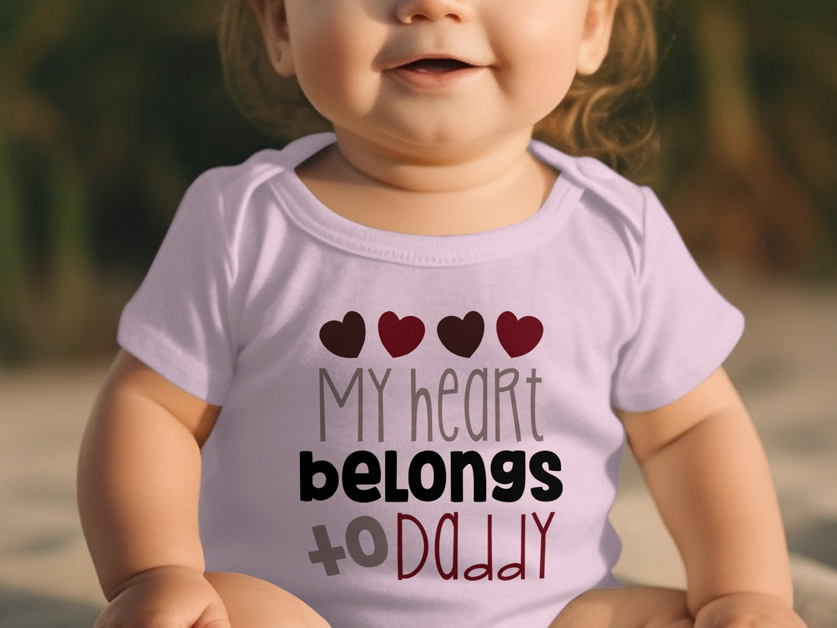 A baby wearing a light pink short-sleeved bodysuit with hearts and the text "My heart belongs to Daddy".