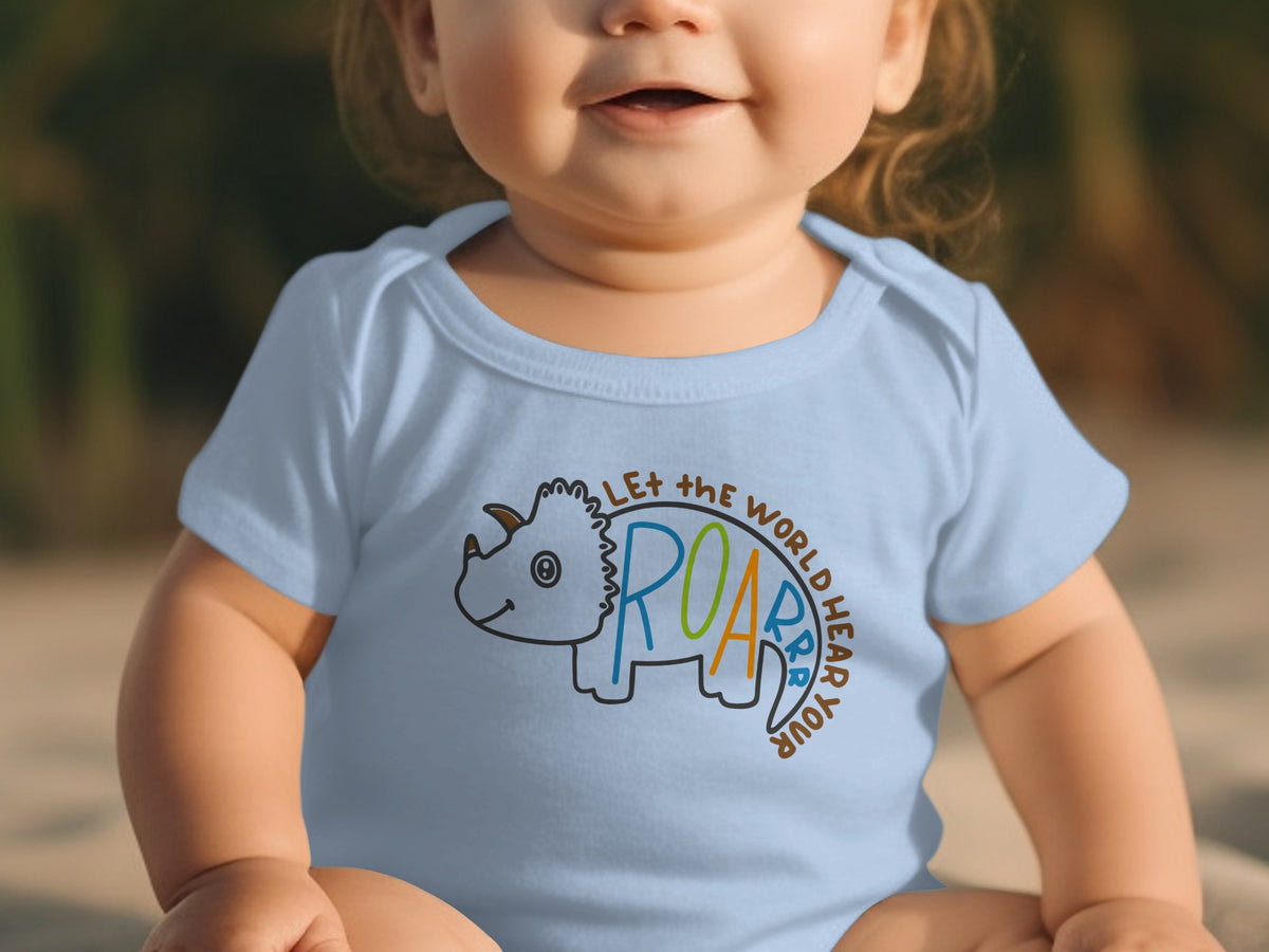 A smiling toddler wearing a light blue bodysuit featuring a cartoon dinosaur and the text "LET THE WORLD HEAR YOUR ROAR".