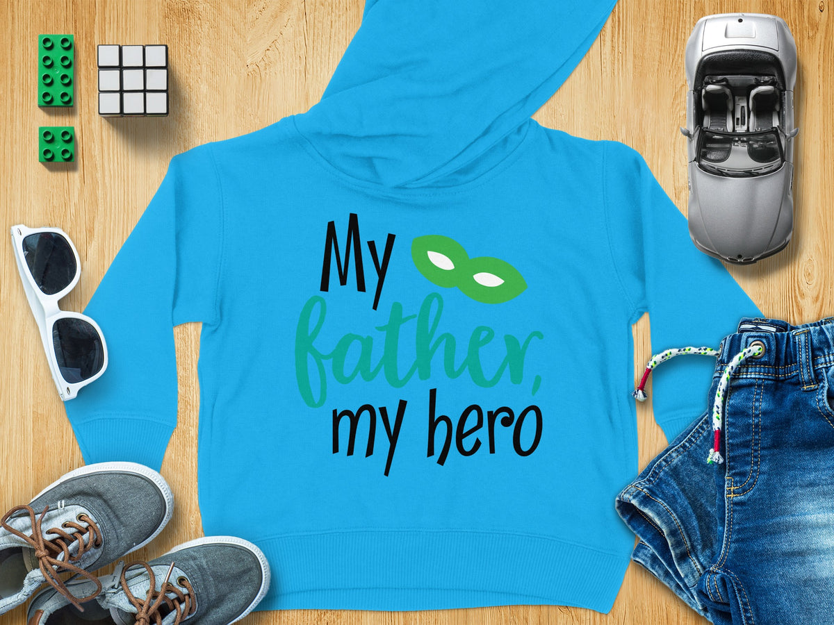 Bright blue children hoodie with the text My father, my hero and a green mask surrounded by toys.