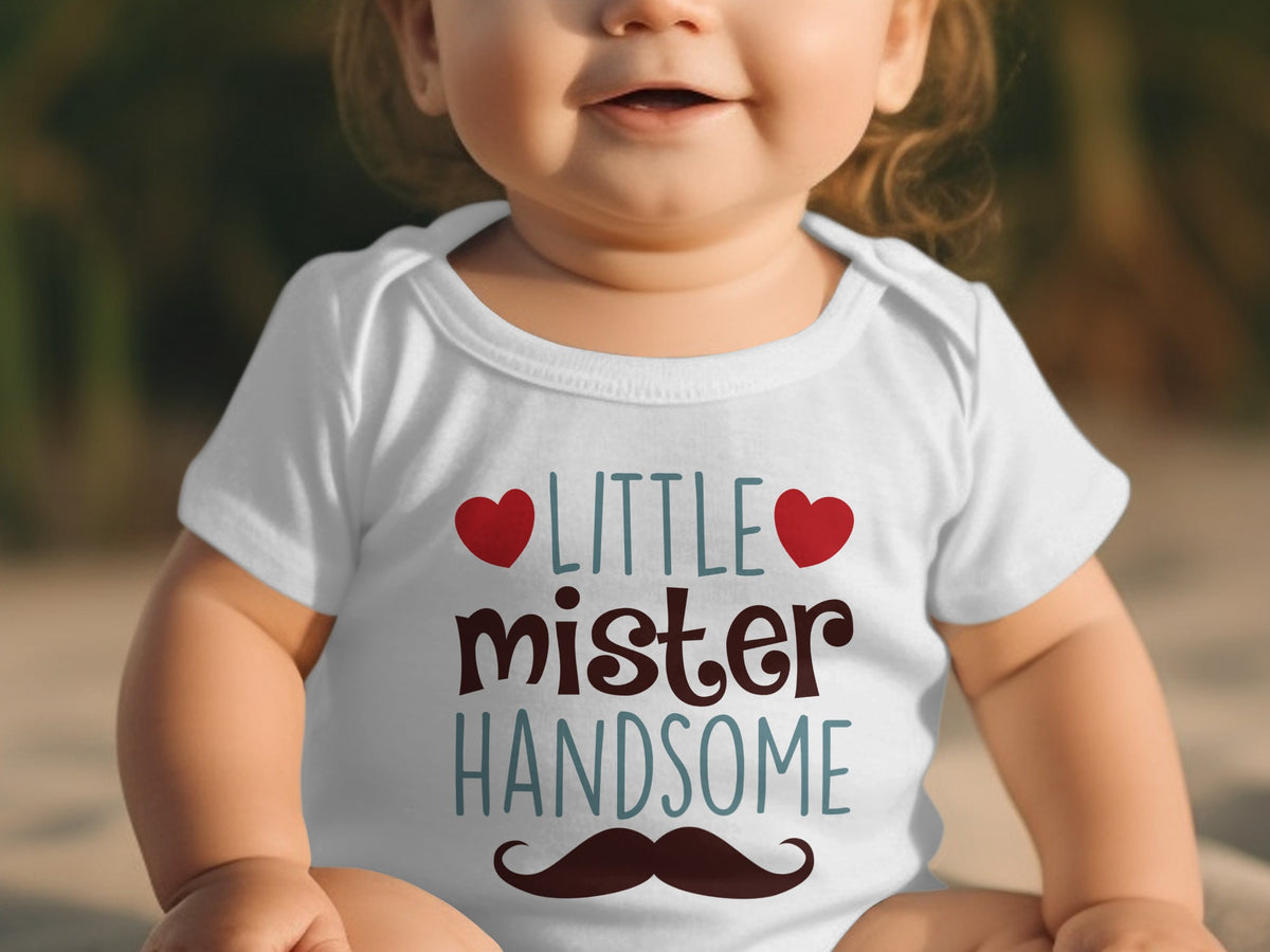 A toddler wearing a white short-sleeve bodysuit featuring the text little mister handsome and a mustache graphic.