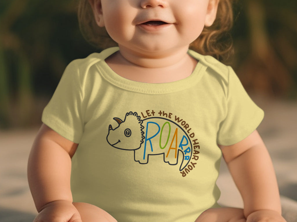 A baby wears a pale yellow bodysuit printed with a triceratops graphic and text.
