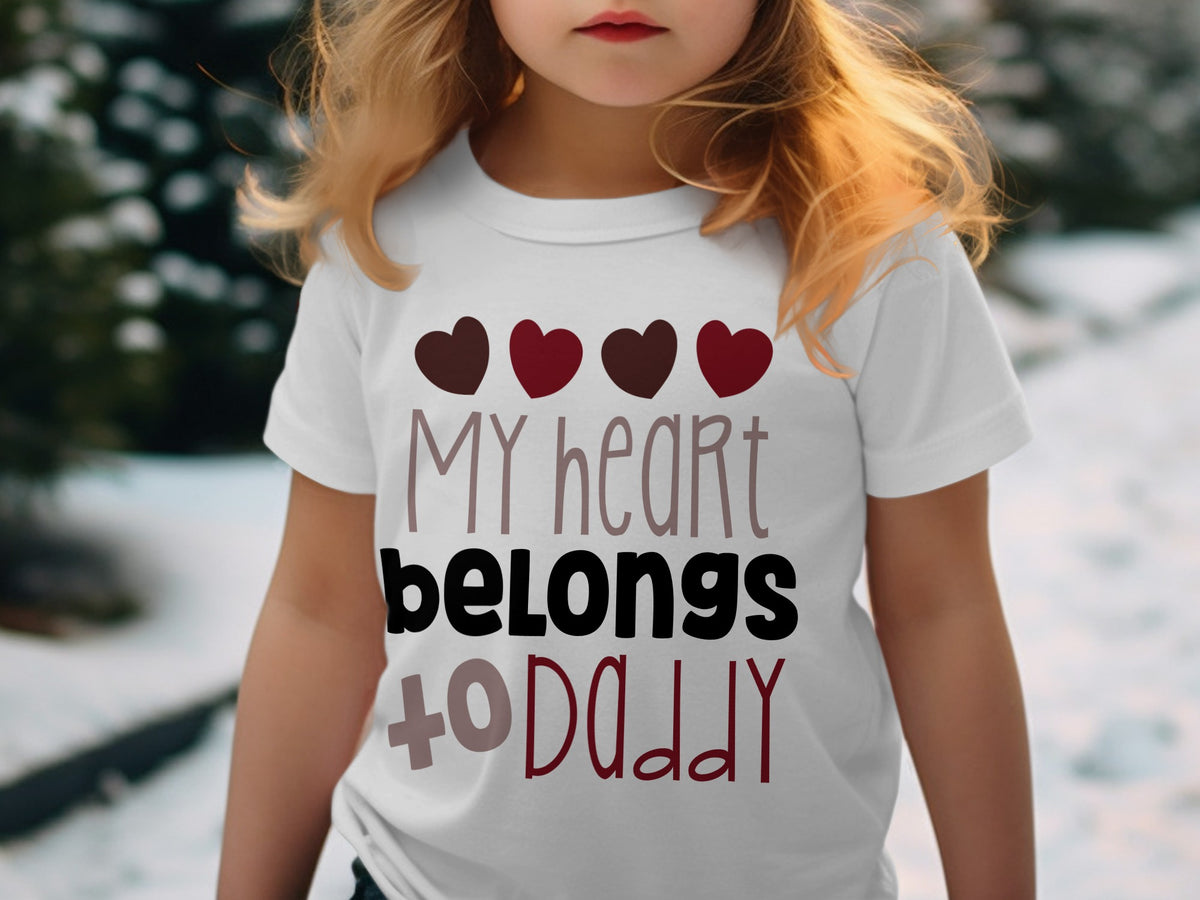 A young blonde child wears a white t-shirt printed with the text MY heart belongs to DADDY and four hearts.
