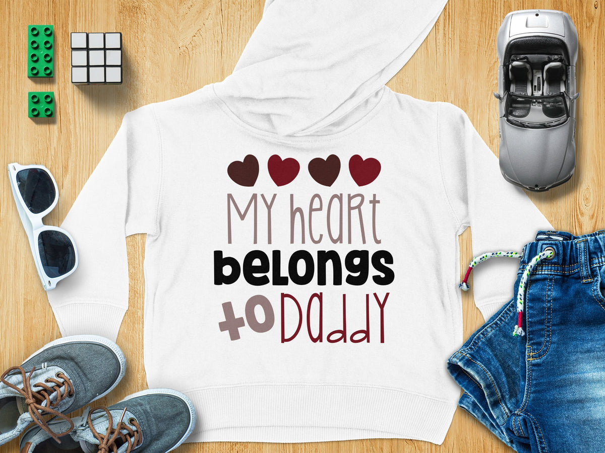 A white hooded sweatshirt with the text My heart belongs to Daddy, surrounded by toys, sunglasses, and denim shorts.