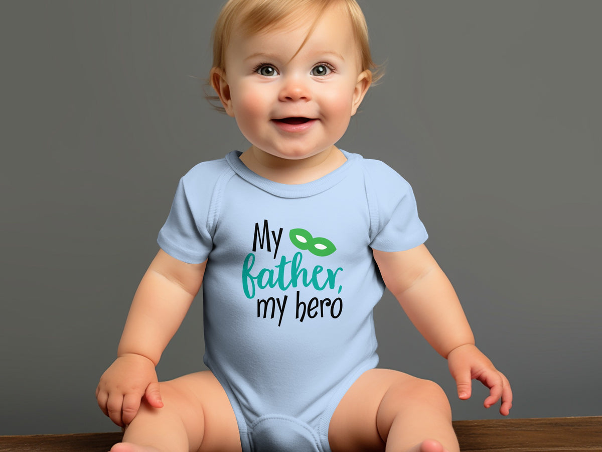A baby sits smiling, wearing a light blue onesie printed with the text My father, my hero.
