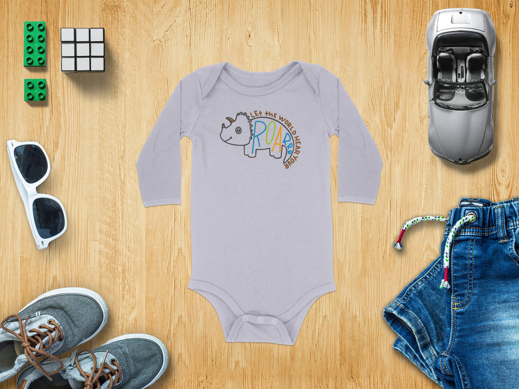 A light purple long-sleeve baby bodysuit with a triceratops graphic, surrounded by toys and clothing on a wooden background.