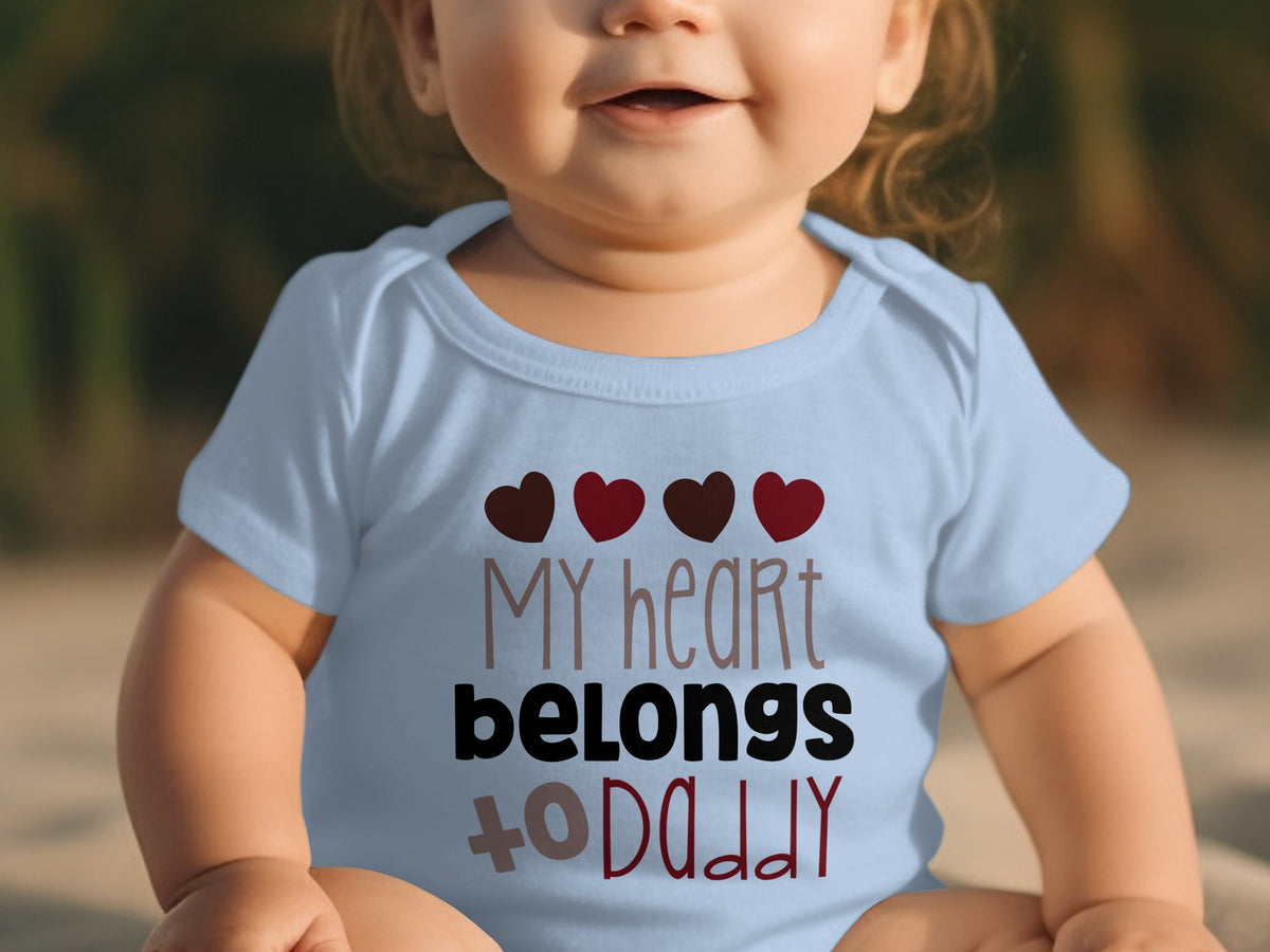 A baby wears a light blue onesie printed with the text My heart belongs to Daddy and four red hearts.