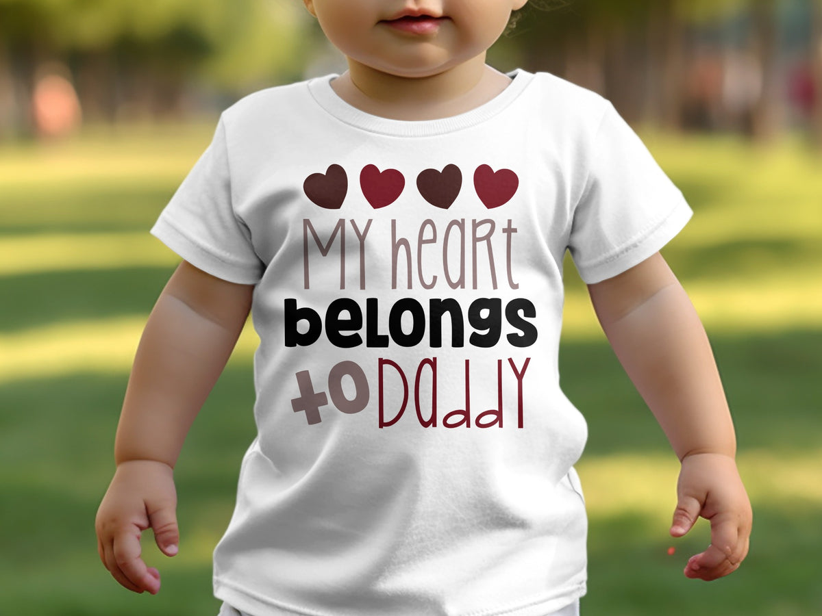 A toddler wearing a white t-shirt printed with four small hearts and the text My heart belongs to Daddy.