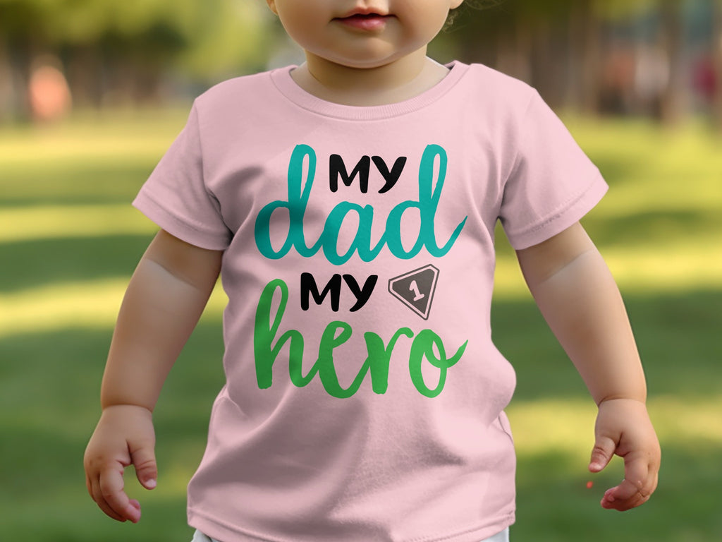 A baby wearing a pink t-shirt with the text My Dad My Hero printed on the chest.