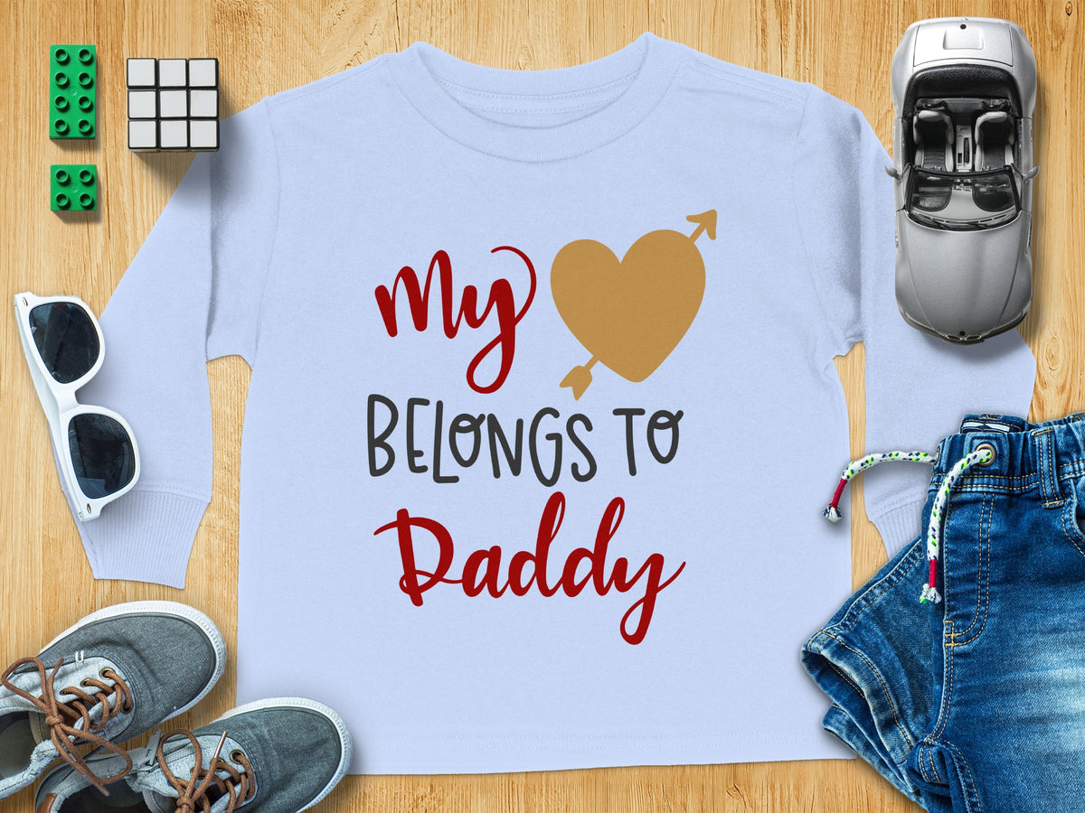 A light blue long-sleeved child's shirt featuring the text My Belongs to Daddy and a heart pierced by an arrow.