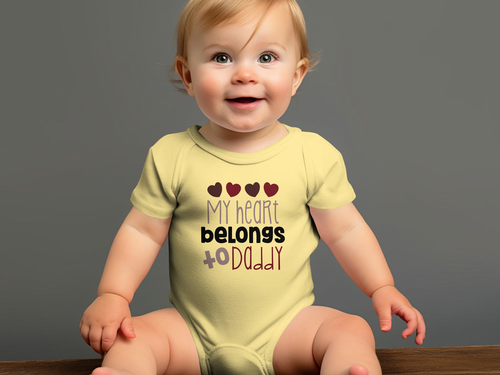 A smiling baby wearing a yellow onesie with the text "my heart belongs to daddy."
