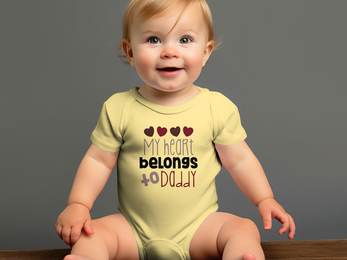 A smiling baby wearing a yellow onesie with the text "my heart belongs to daddy."