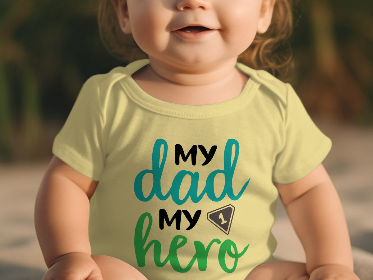 A baby wearing a yellow bodysuit printed with the text my dad my hero in black and teal.
