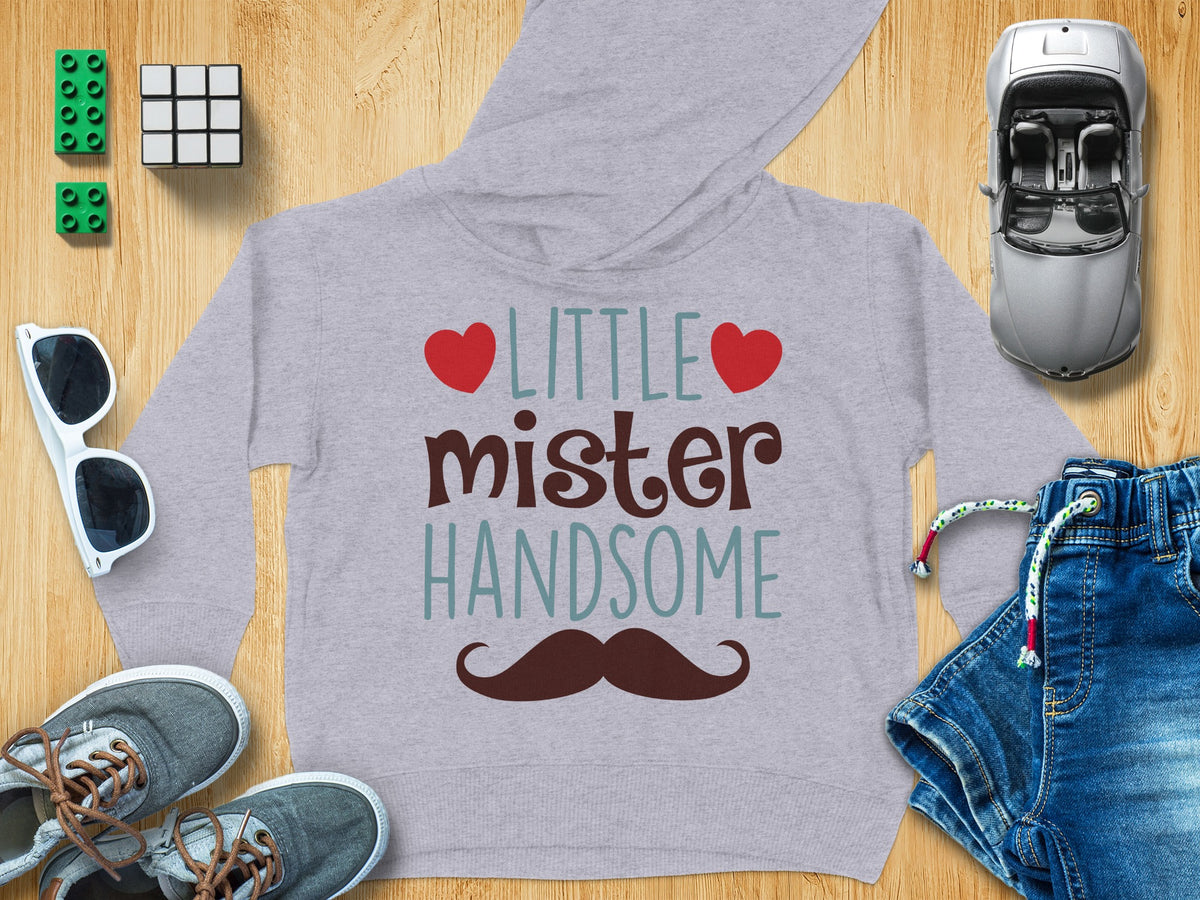 Gray children's hoodie with the text LITTLE mister HANDSOME and a mustache, surrounded by toys and accessories.