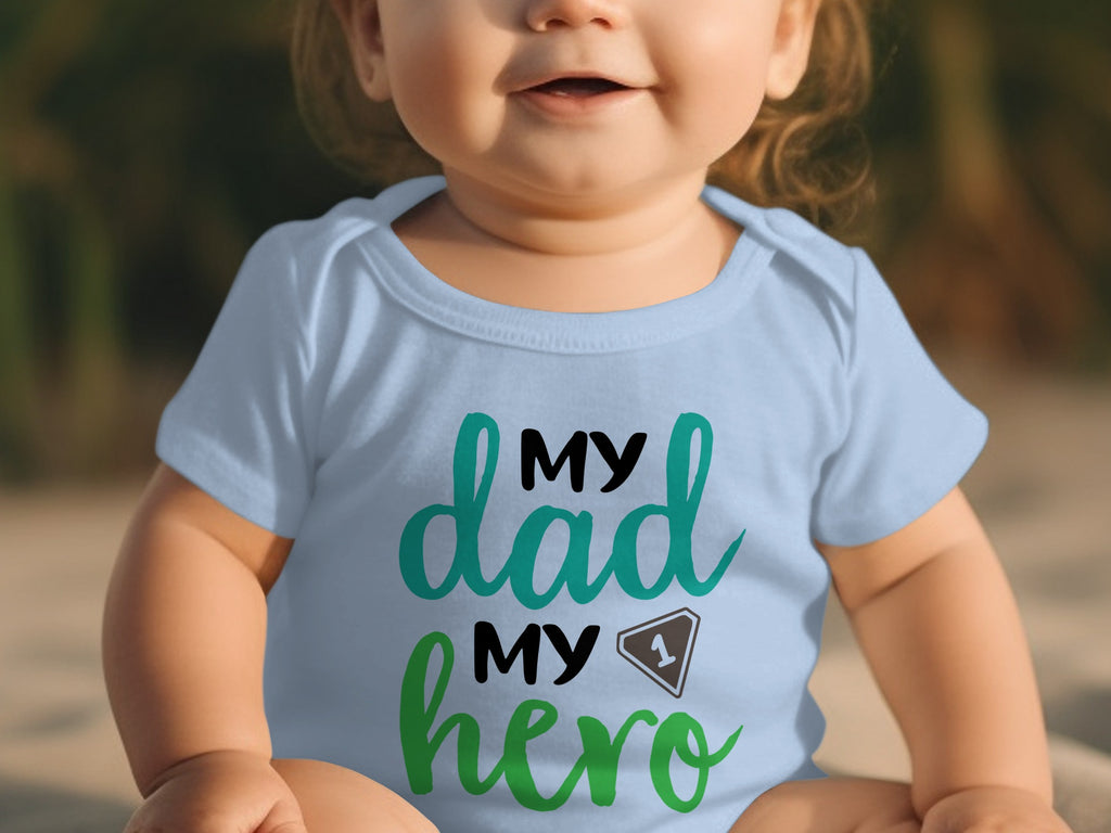 A light blue baby bodysuit featuring the green and black text "MY dad MY hero".