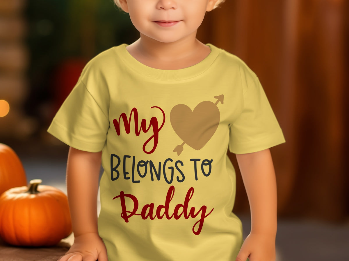 A toddler wearing a yellow t-shirt printed with the text My Heart Belongs to Daddy.