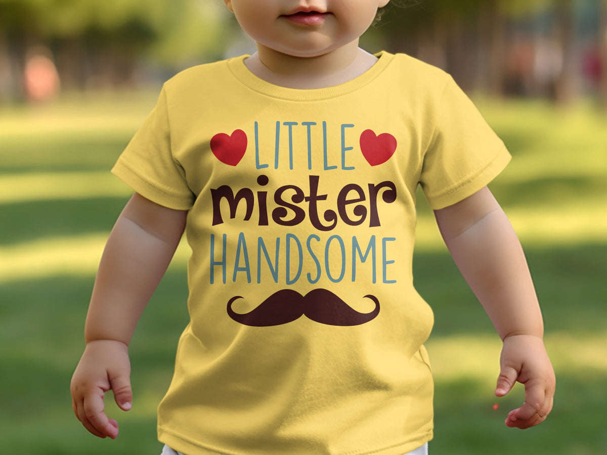 A toddler wears a yellow t-shirt printed with the text LITTLE mister HANDSOME and a mustache.