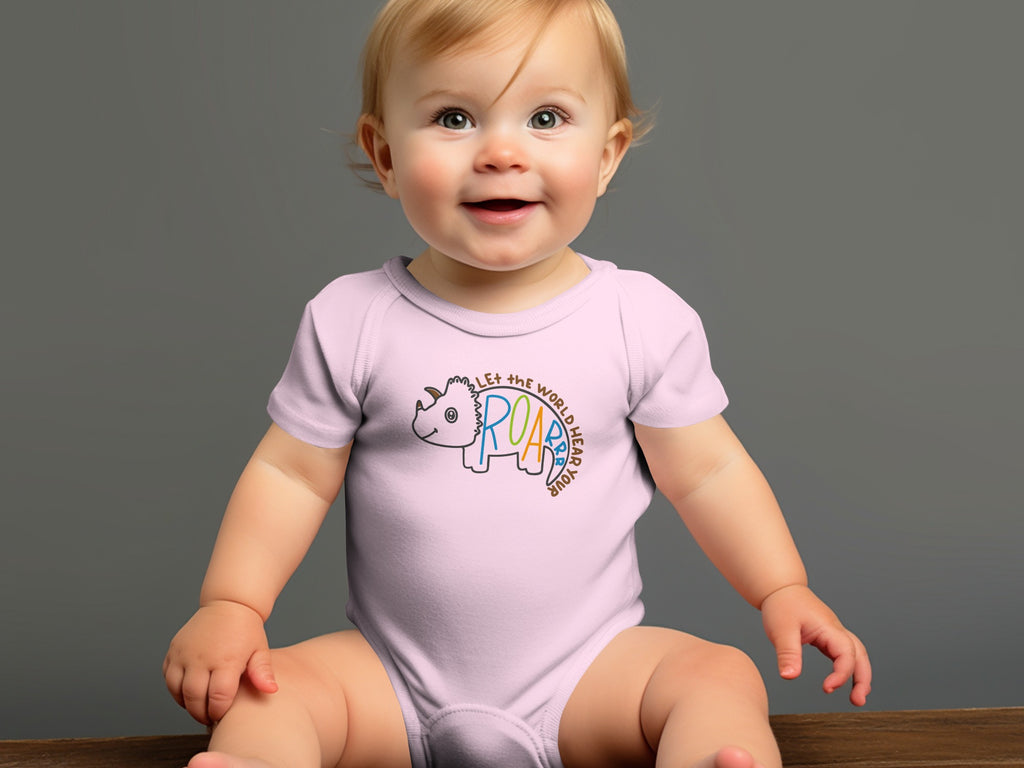 A smiling baby sits wearing a light pink onesie printed with a triceratops and text.