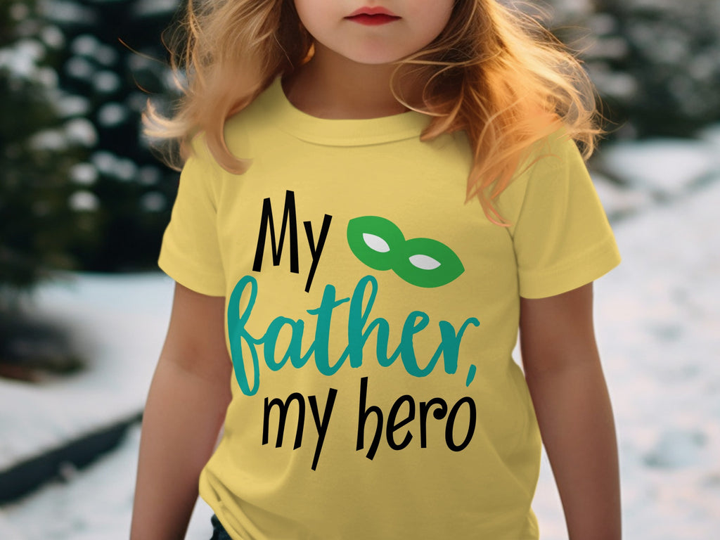 A young child wearing a yellow t-shirt printed with the text "My father, my hero" and a green hero mask.