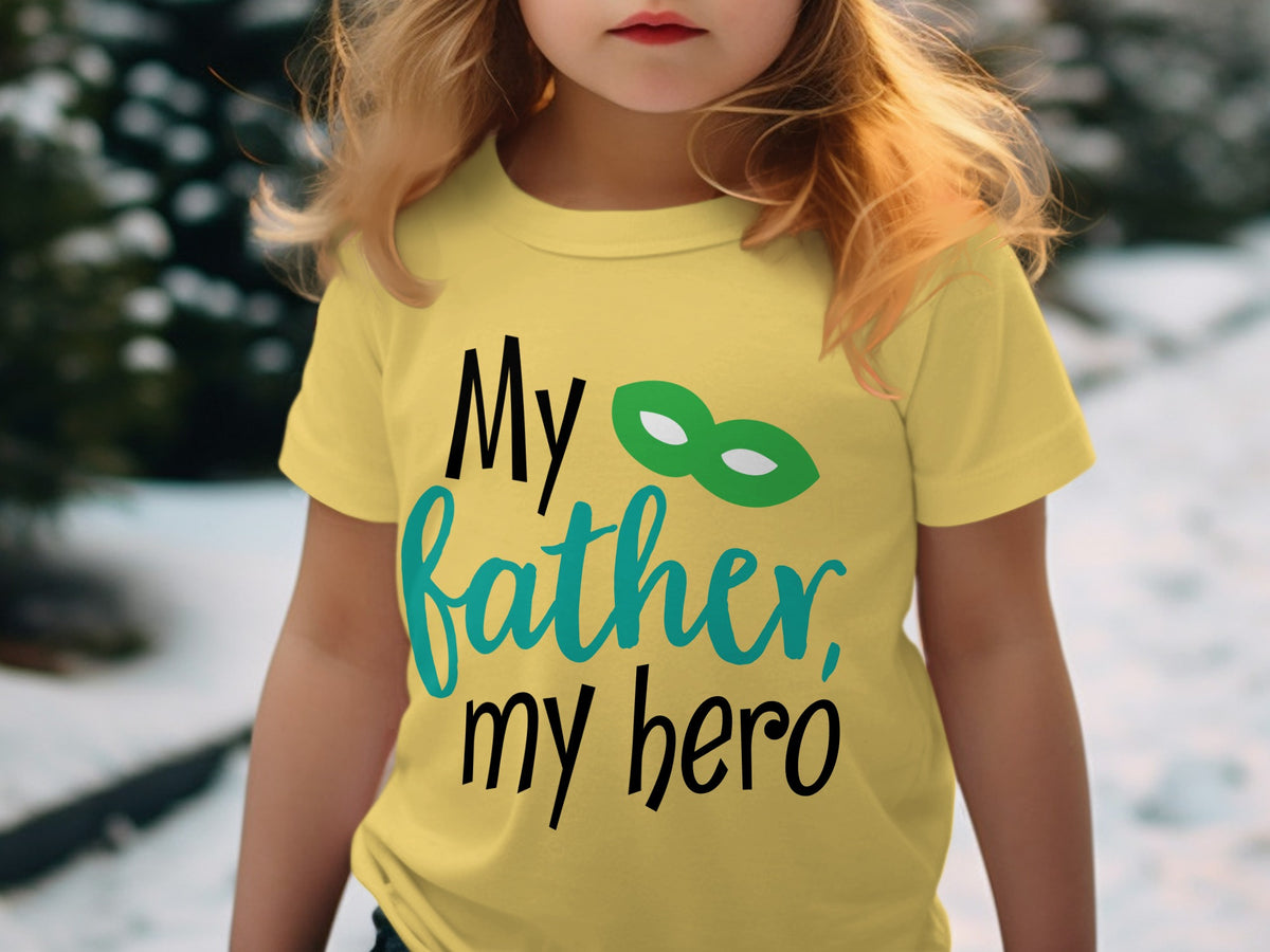 A young child wearing a yellow t-shirt printed with the text "My father, my hero" and a green hero mask.
