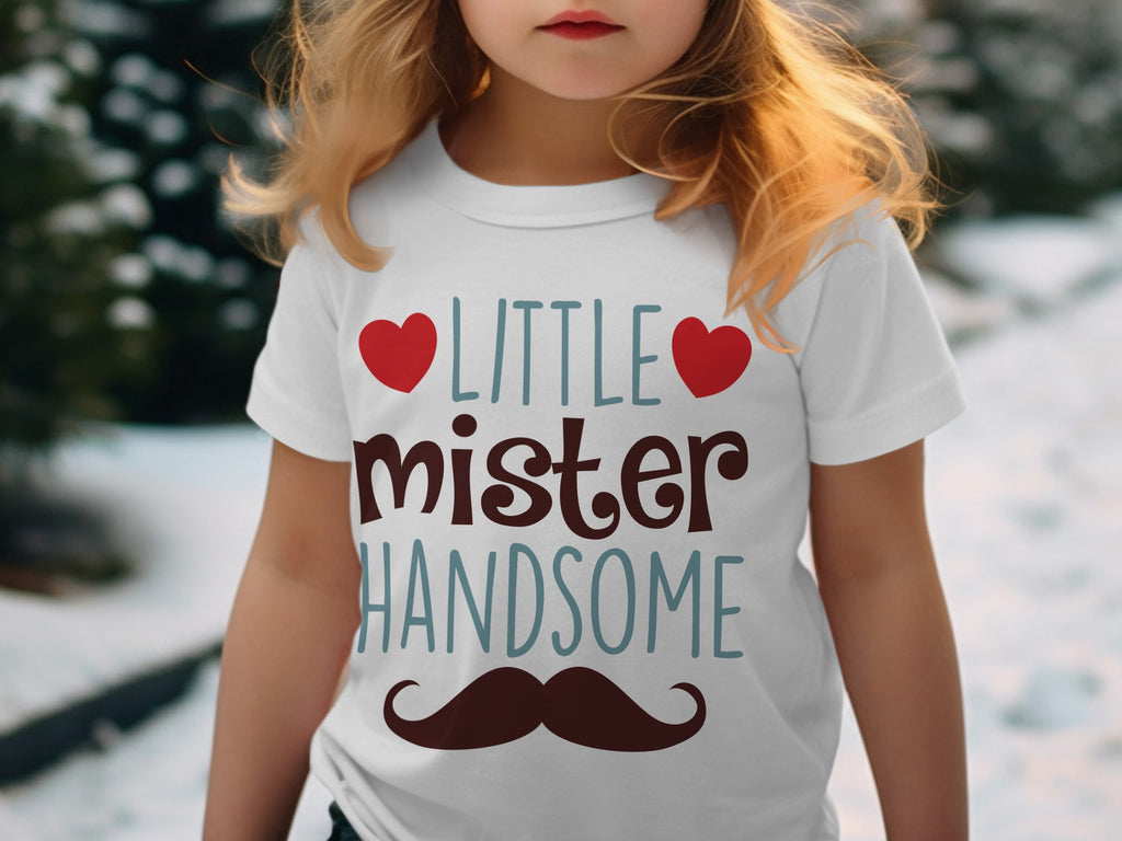 A child wears a white t-shirt printed with the words Little Mister Handsome flanked by red hearts and a brown mustache.