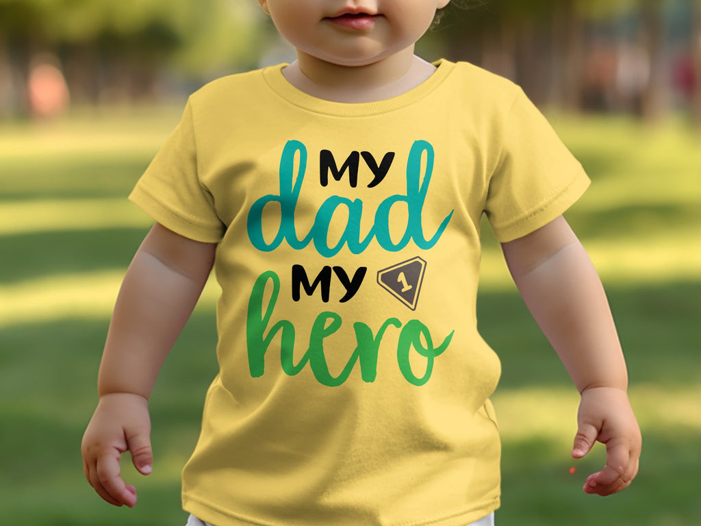 A toddler wears a yellow t-shirt printed with the text "My dad, my hero".