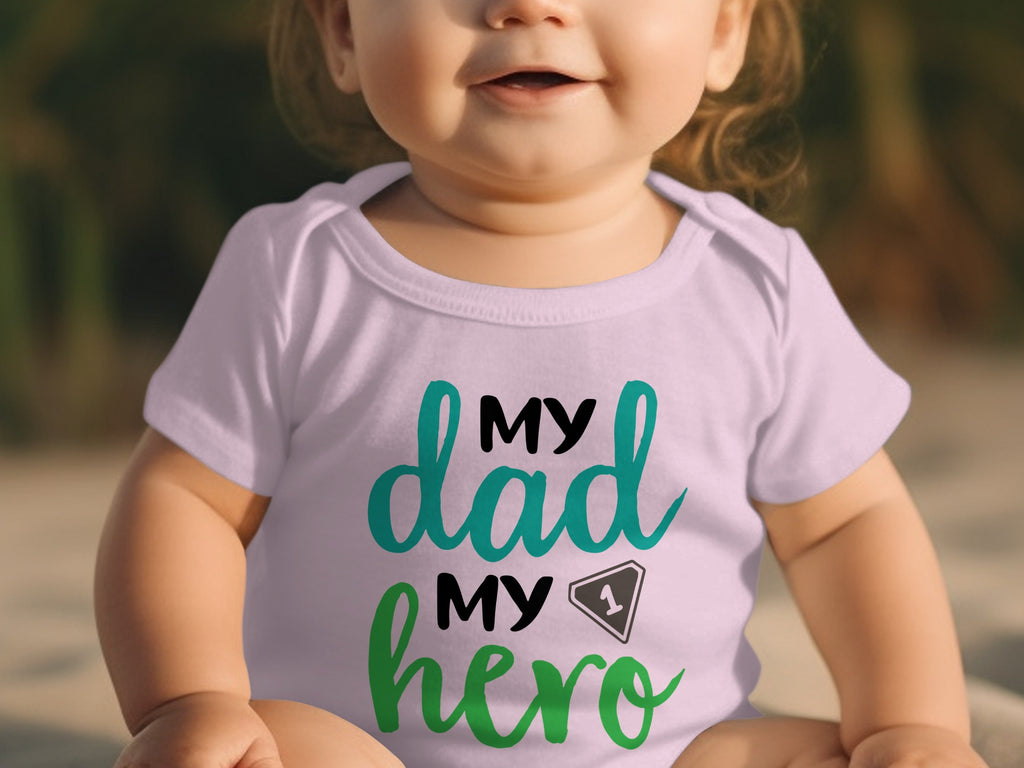 A smiling baby wears a light purple bodysuit with the text "MY dad MY hero" and a number one graphic.