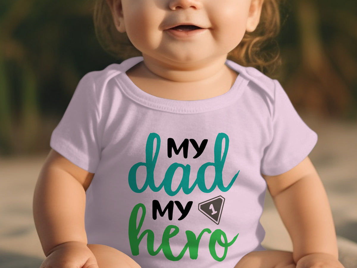 A smiling baby wears a light purple bodysuit with the text "MY dad MY hero" and a number one graphic.