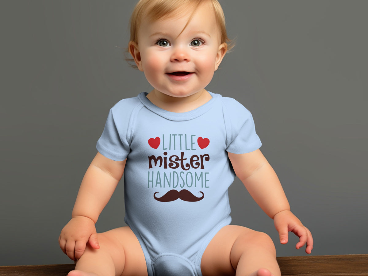 A smiling baby with blonde hair sits wearing a light blue onesie with text and a mustache graphic.