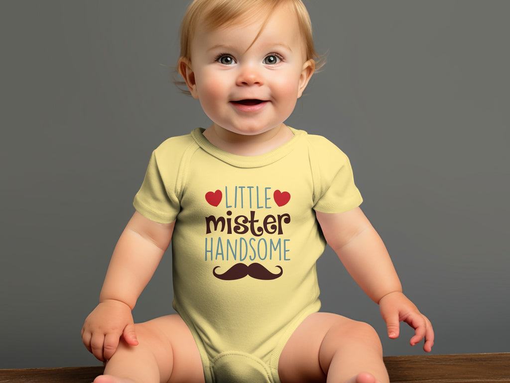 A smiling baby sits wearing a yellow onesie printed with the text Little Mister Handsome and a mustache graphic.